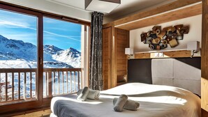 A hotel room with a large window offering a mountain view, a bed with a headboard, and a wall-mounted wooden art piece. - Résidence Koh-I Nor by Les Etincelles (Les Belleville)