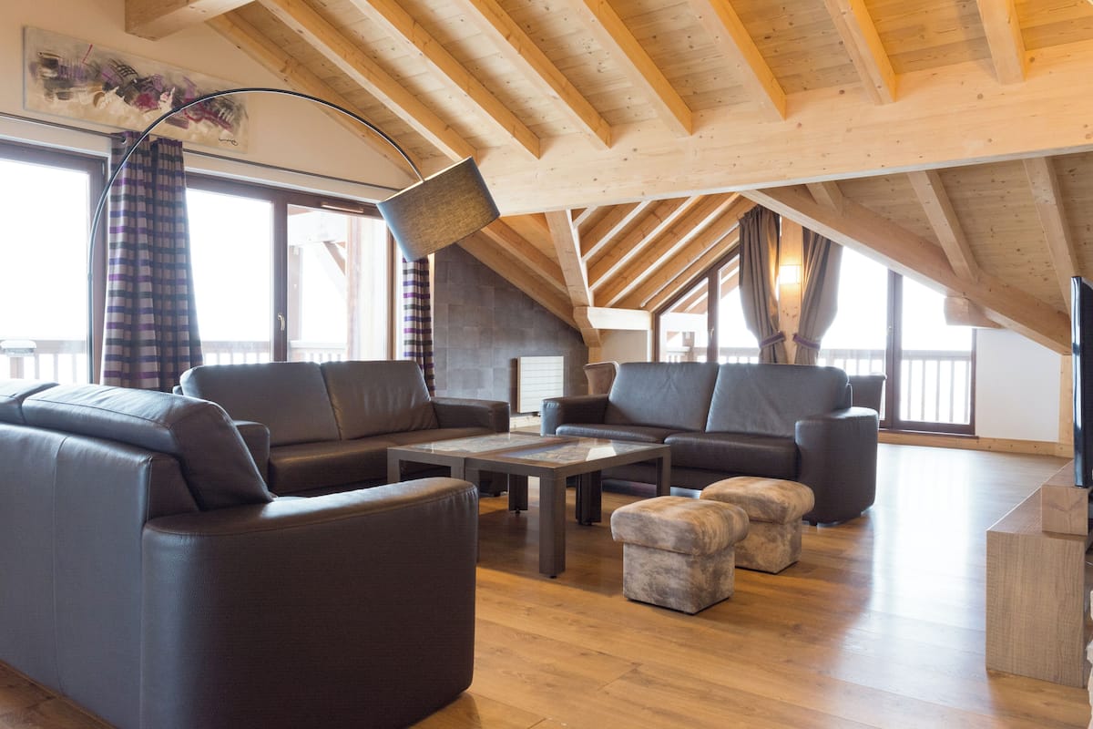 A spacious loft with high ceilings, exposed wooden beams, and large windows.