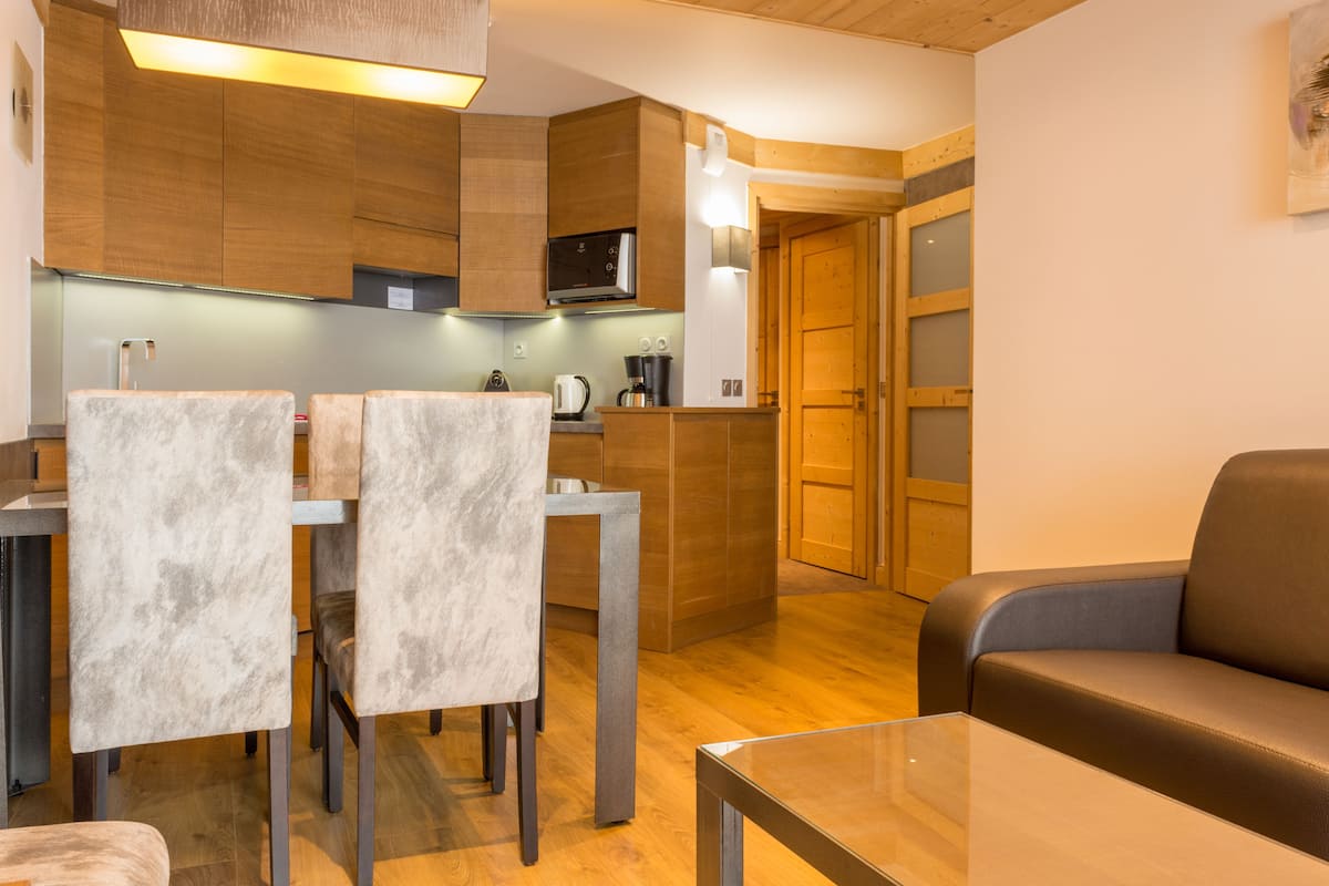A modern kitchen with wooden cabinets, a microwave, and a dining area with two chairs and a table.