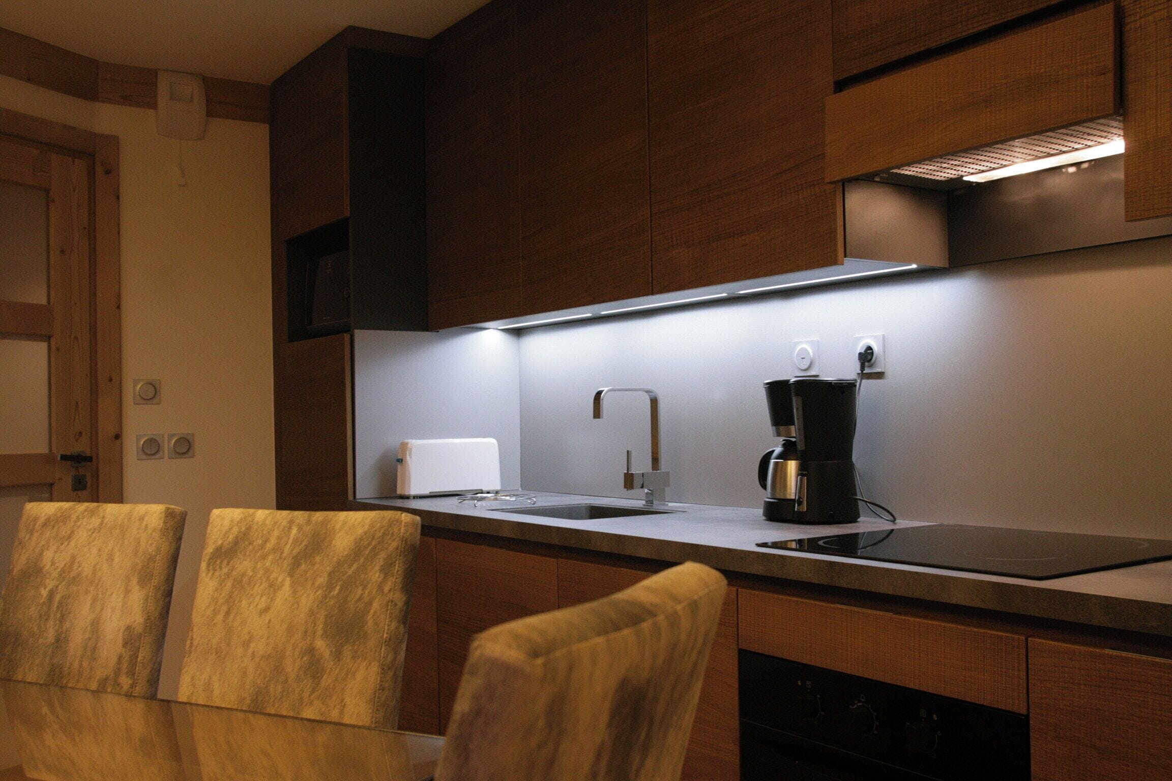 A modern kitchen with wooden cabinets, a stainless steel countertop, a coffee maker, and a built-in oven.