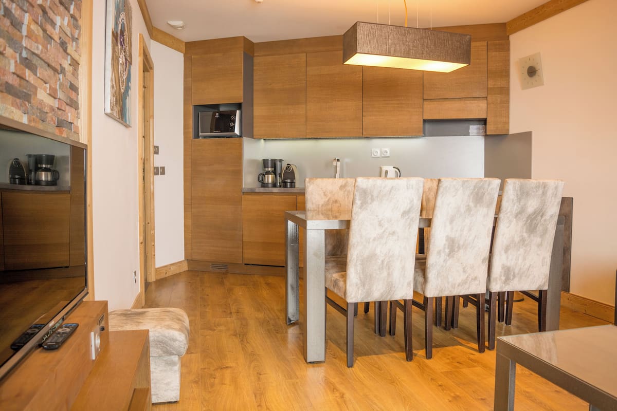 A modern kitchen with wooden cabinets, a dining area with a table and chairs, and a built-in TV.