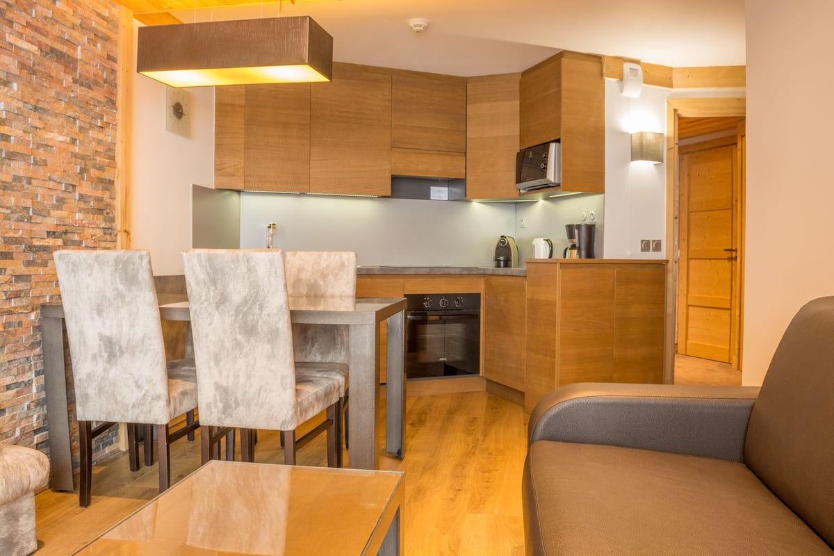 A compact kitchen with wooden cabinets, a built-in oven, and a dining area with a table and chairs.