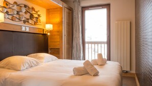 A hotel room with a large bed, a wooden headboard, a wall-mounted light fixture, and a window with curtains. - Résidence Koh-I Nor by Les Etincelles (Les Belleville)