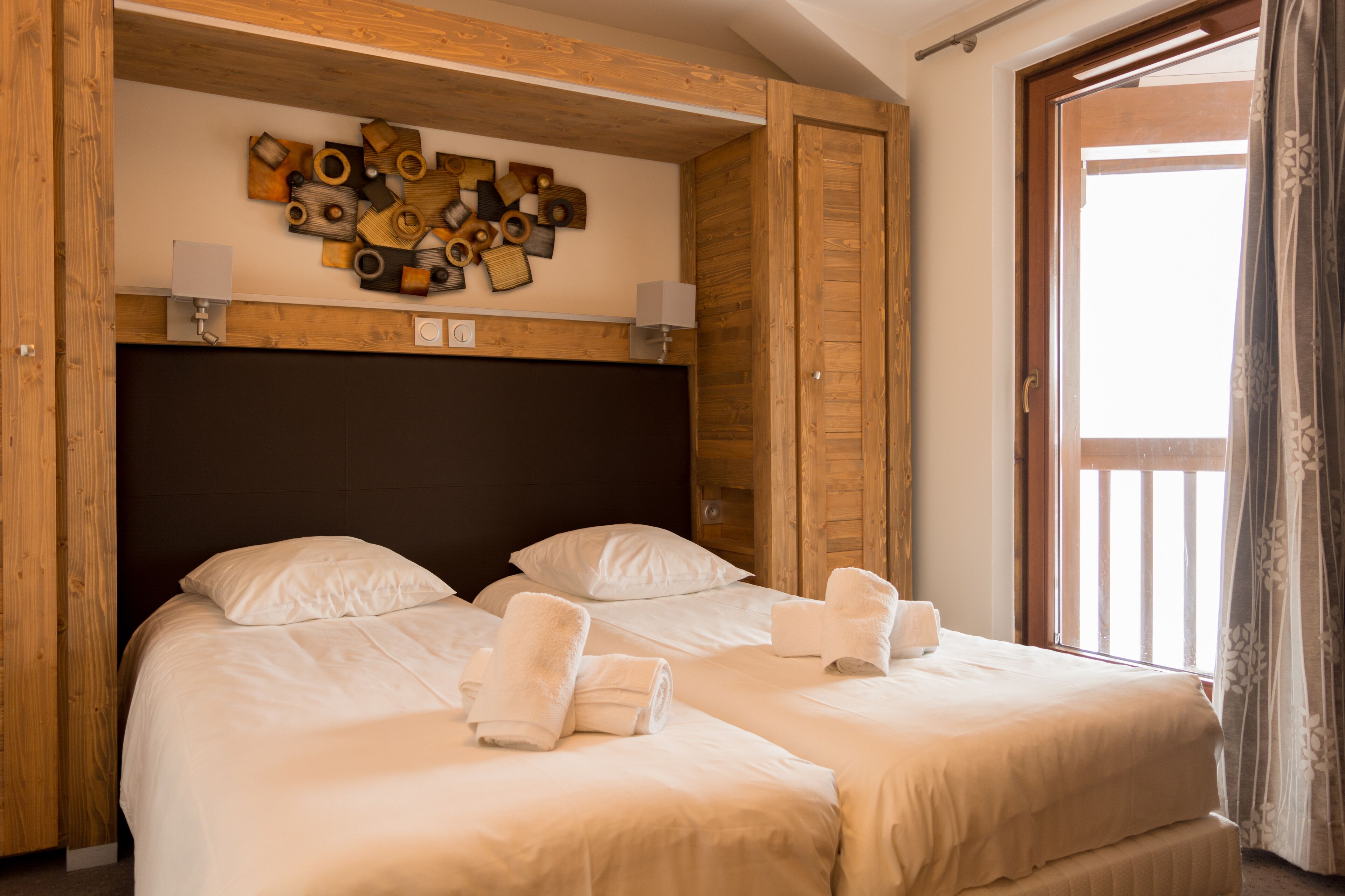 Habitación de hotel con dos camas, cabeceros de madera, una obra de arte en la pared y una ventana con cortinas.