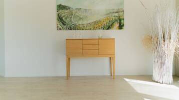 Habitación minimalista con una consola de madera, un cuadro abstracto grande y una alta jarra blanca con plantas secas.