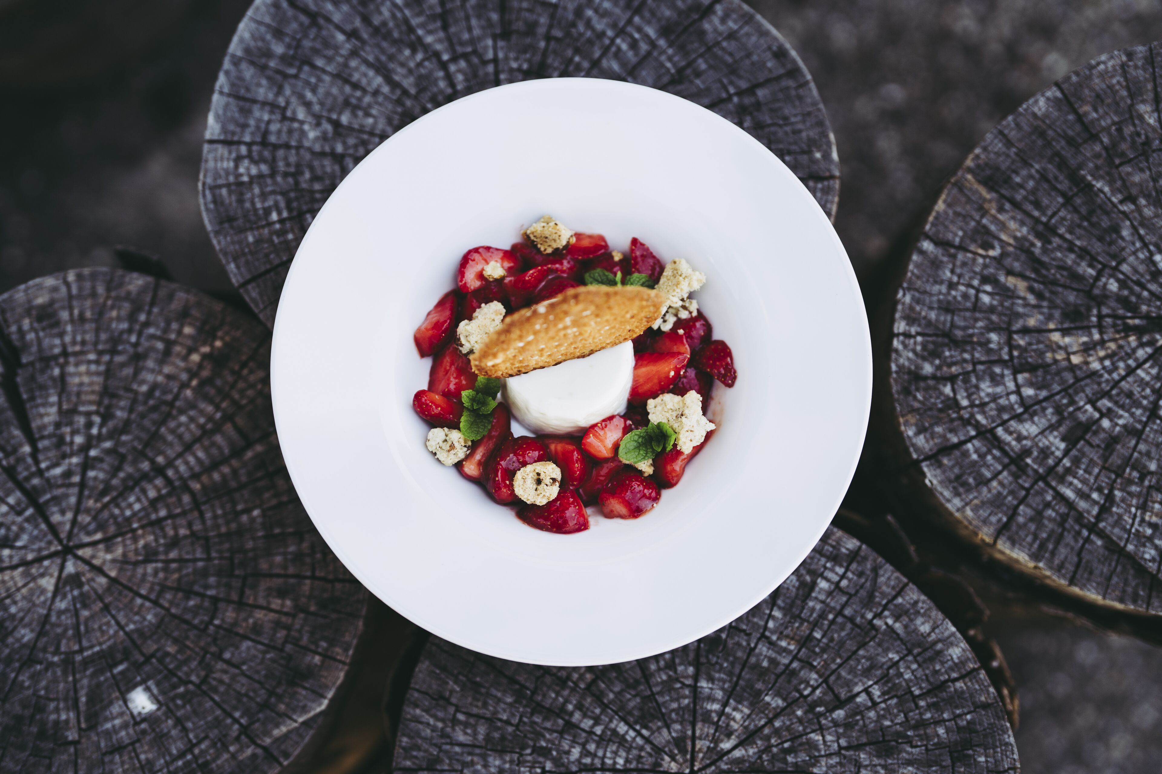 Un plato blanco con un postre de fresas, una porción de helado y un pastel sobre una mesa de madera.
