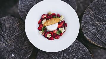 Un plato blanco con un postre de fresas, una porción de helado y un pastel sobre una mesa de madera.