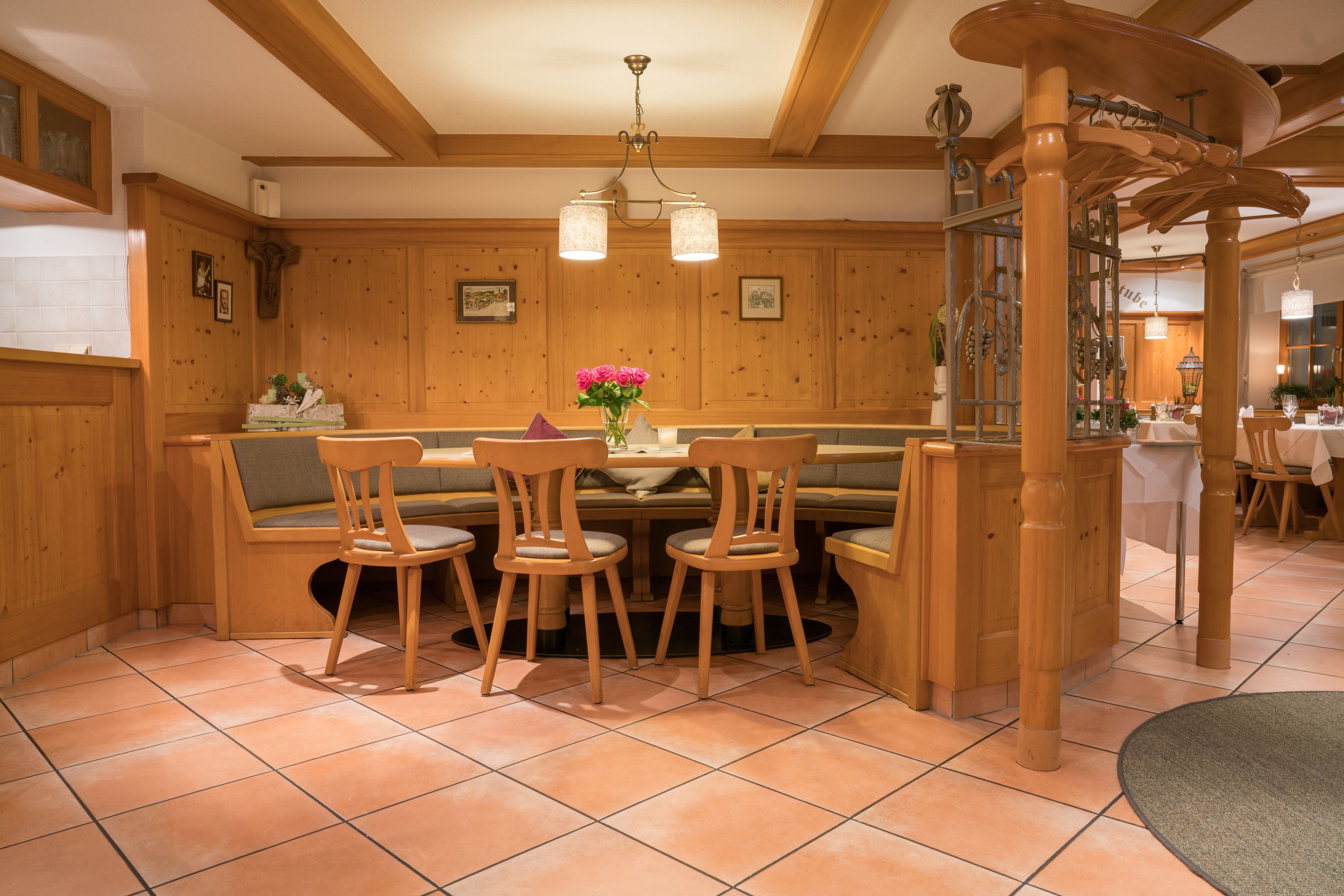 A wooden interior with a round table and chairs, a bench, and a decorative wooden arch.
