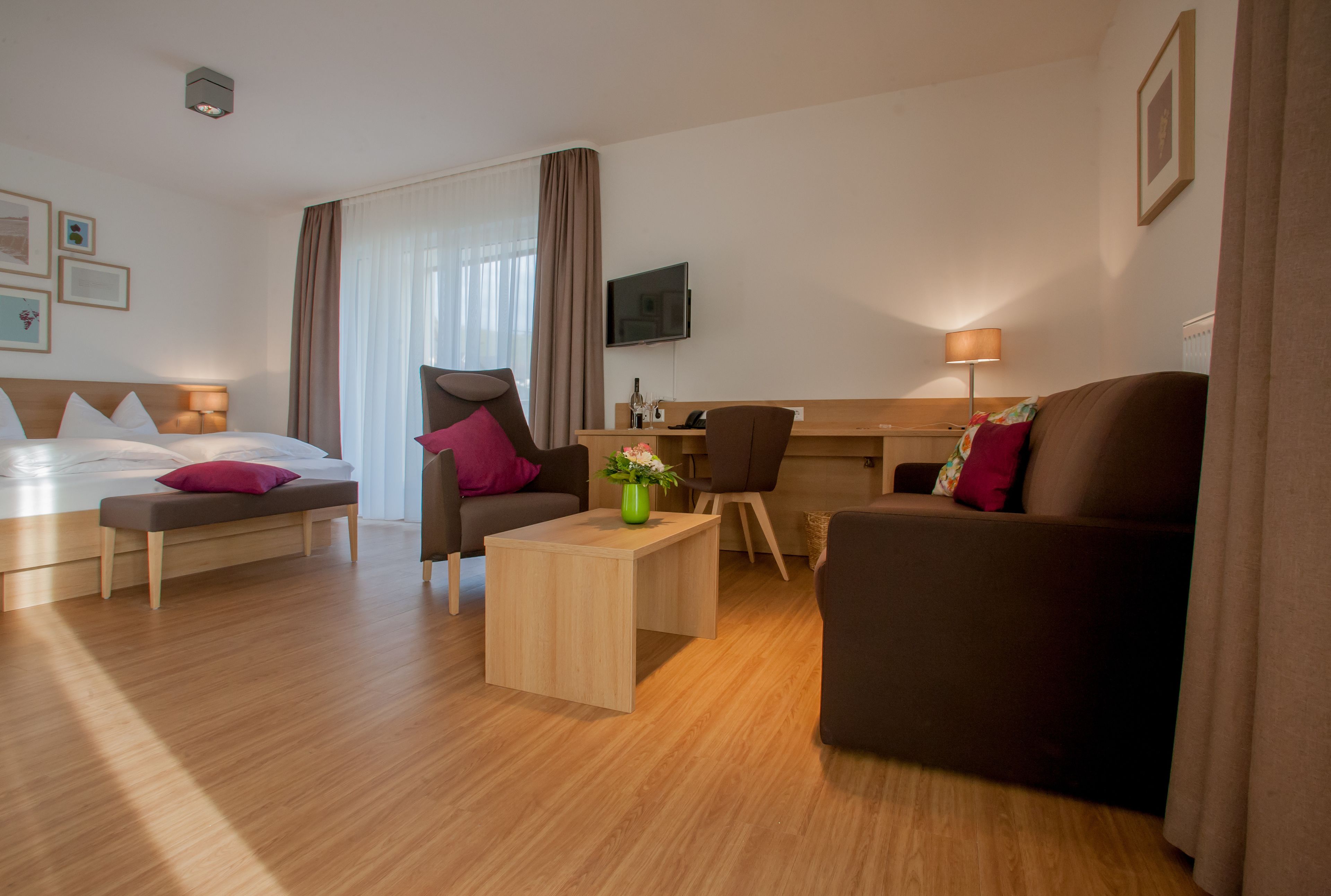 A hotel room with a bed, a sofa, a desk, a chair, a TV, and a lamp.