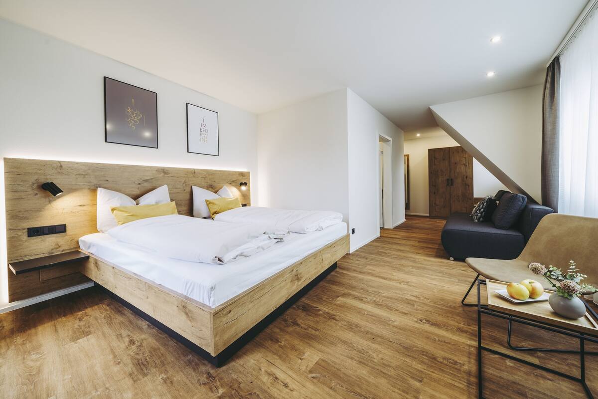 A modern bedroom with a wooden bed, a sofa, and a small table with apples and flowers.
