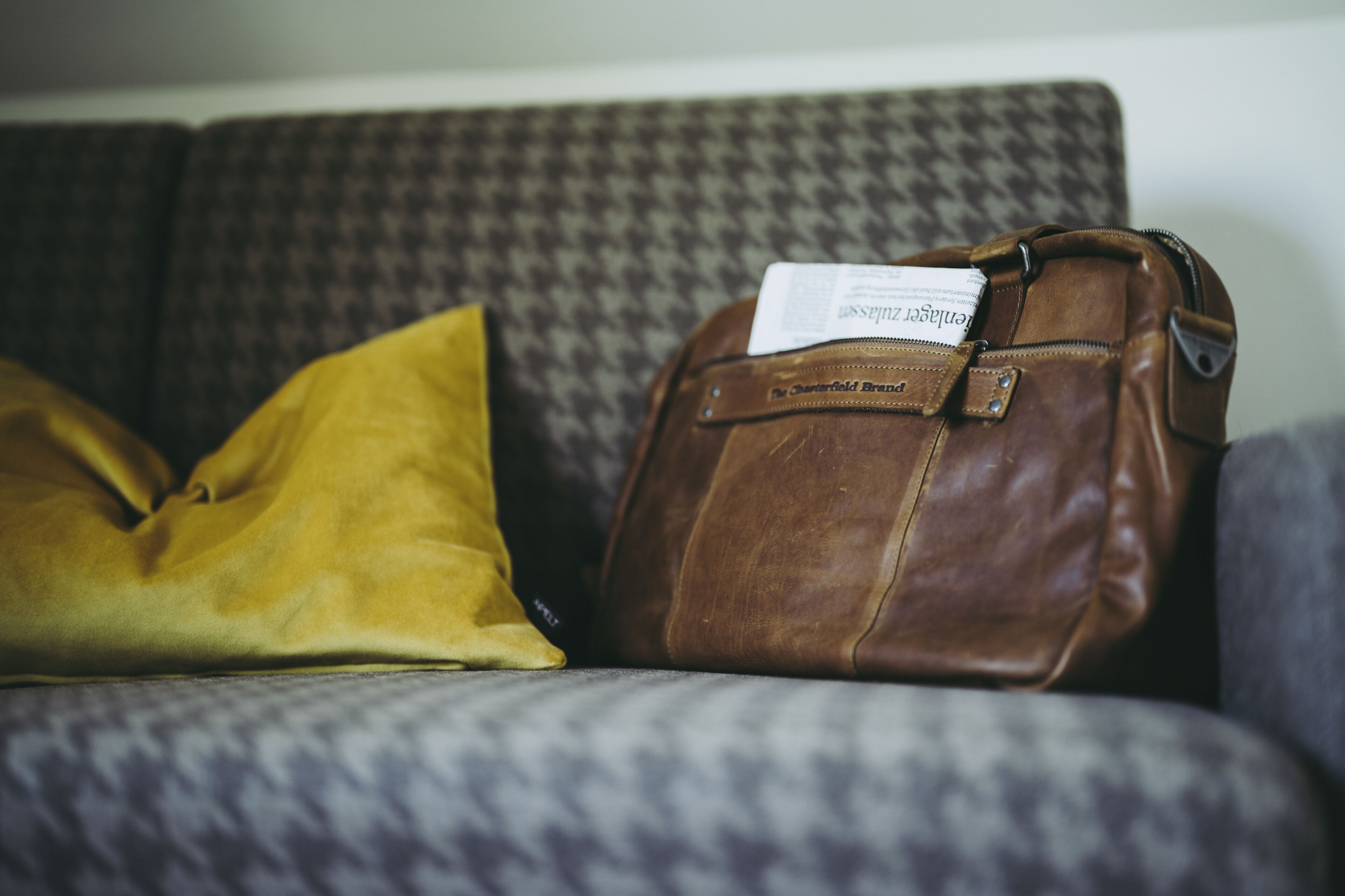 A brown leather bag with a label on a patterned couch.