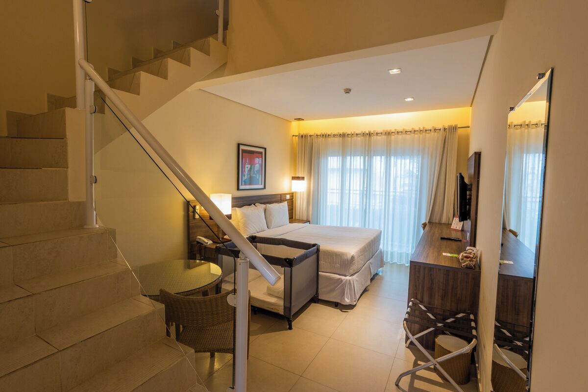Habitación de hotel con cama, escritorio, silla, una mesita, televisión y una escalera.
