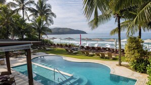 A pool with a curved edge, surrounded by lounge chairs and umbrellas, with a view of the ocean and a distant island. - Amora Hotel (São Sebastião)