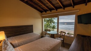 A hotel room with two beds, a small table, a chair, a TV, and a view of the beach. - Amora Hotel (São Sebastião)