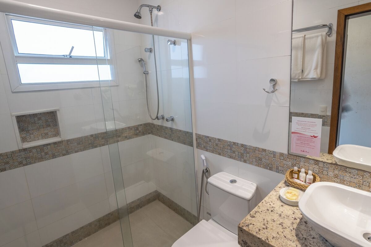 A bathroom with a glass-enclosed shower, a toilet, a sink, and a window.