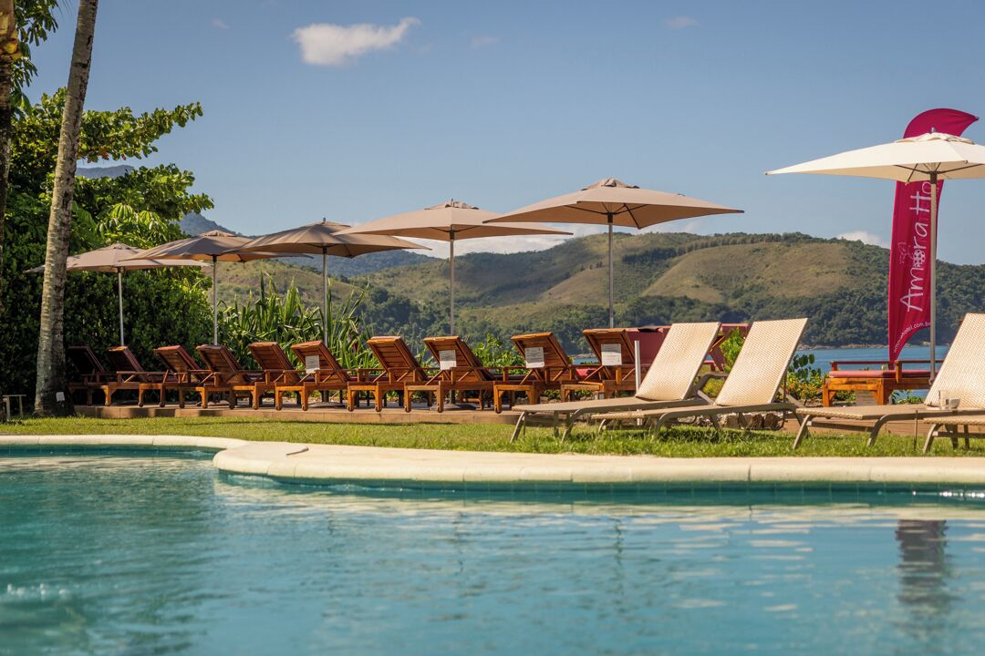 A poolside area with lounge chairs and umbrellas, a clear sky, and a mountainous backdrop.