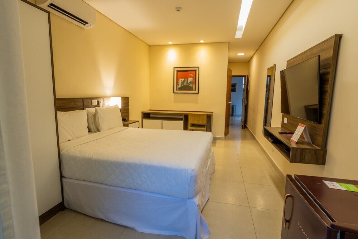 A hotel room with a bed, a desk, a TV, and a mirror.