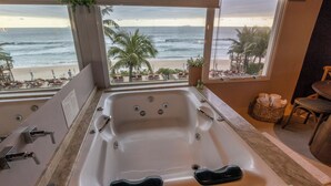 A bathroom with a large bathtub, a sink, and a view of the beach. - Amora Hotel (São Sebastião)