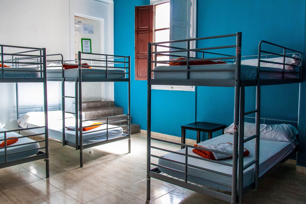 A dormitory room with bunk beds, a small table, and a window with a view of the outside.