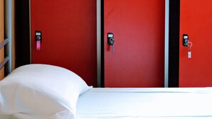 A hotel room with a bed, white bedding, and a red wall with three black locks. - Home Backpackers Valencia by Feetup Hostels (Valencia)