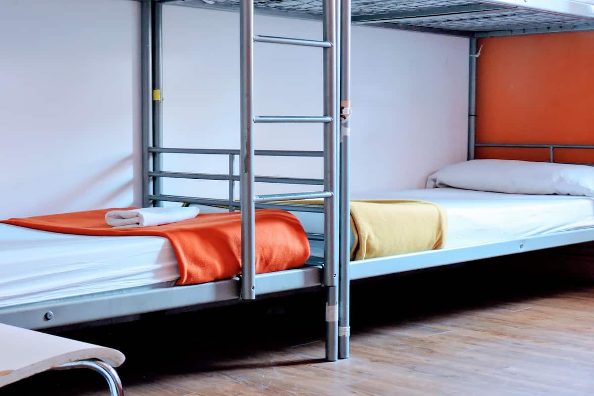 A bunk bed with a ladder, a single bed with a yellow blanket, and a chair.
