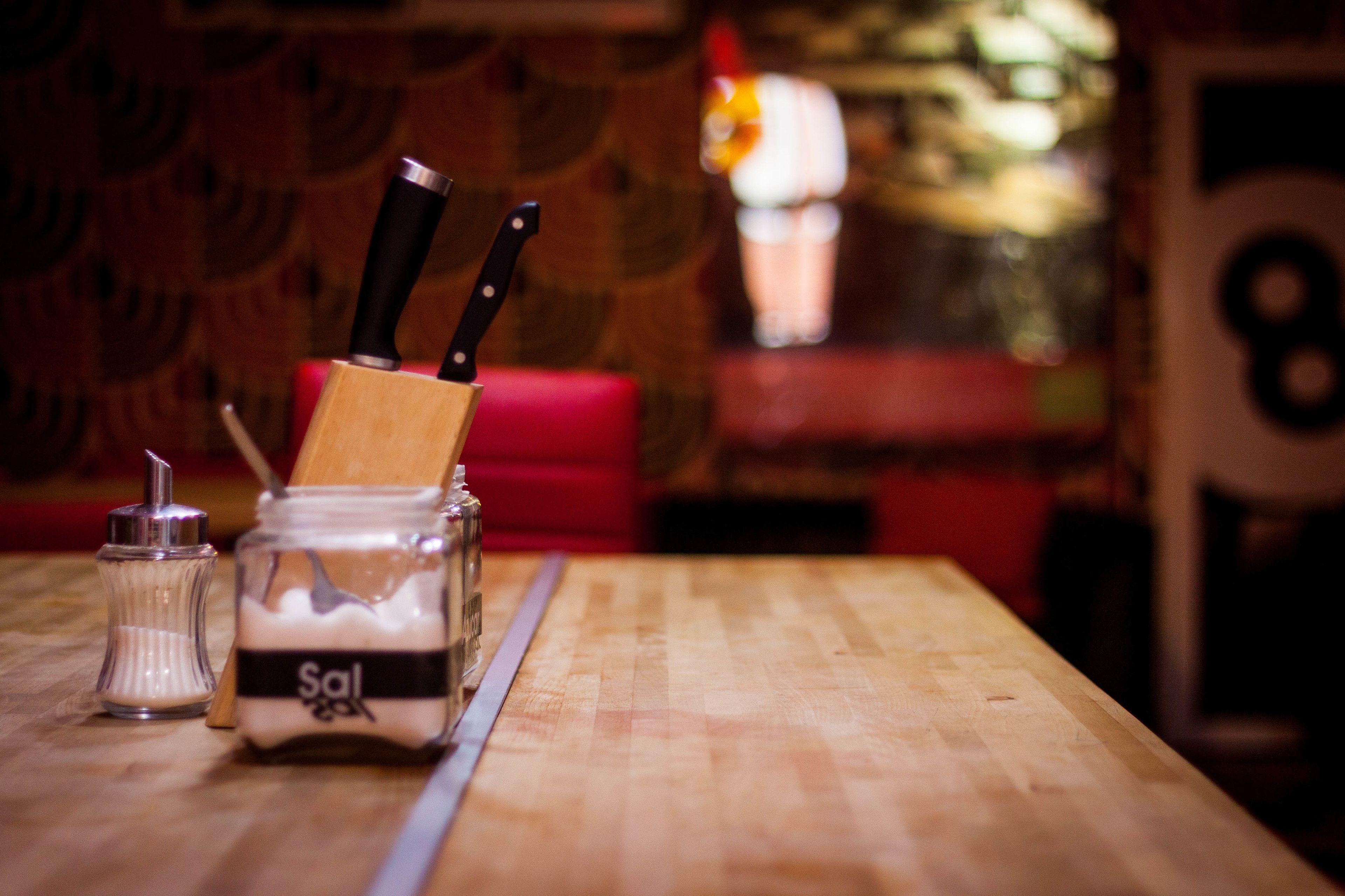 A wooden table with a salt shaker, a jar of salt, and two knives.