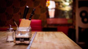 A wooden table with a salt shaker, a jar of salt, and two knives.