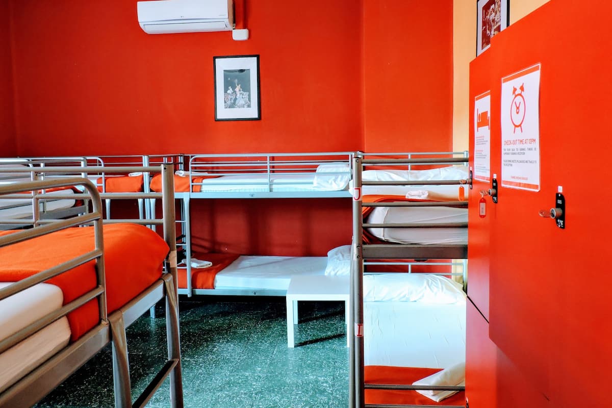 A room with bunk beds, an air conditioner, a framed picture, and a check-out time sign.