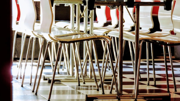A row of white plastic chairs with metal legs and a wooden table in a dining area with a checkered floor. - Home Backpackers Valencia by Feetup Hostels (Valencia)