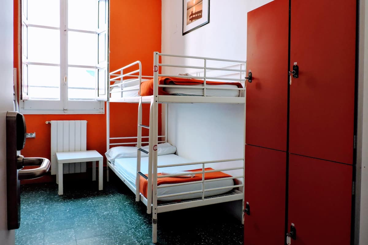 A bunk bed room with a window, a radiator, a small table, and red lockers.