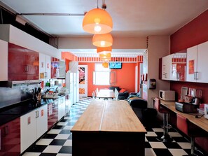 A kitchen with a checkered floor, a wooden island, and a dining area with a TV in the background. - Home Backpackers Valencia by Feetup Hostels (Valencia)