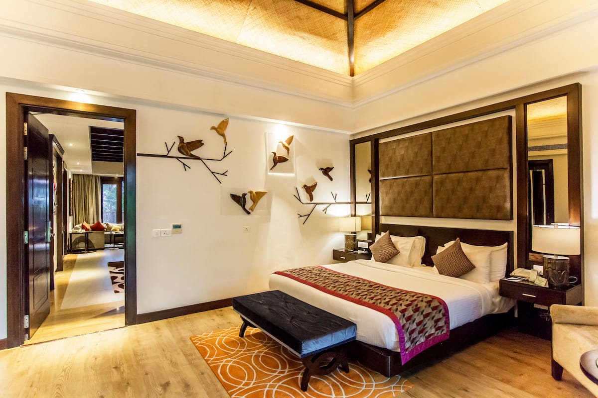 A modern hotel room with a large bed, a bench, a mirror, and wall art.
