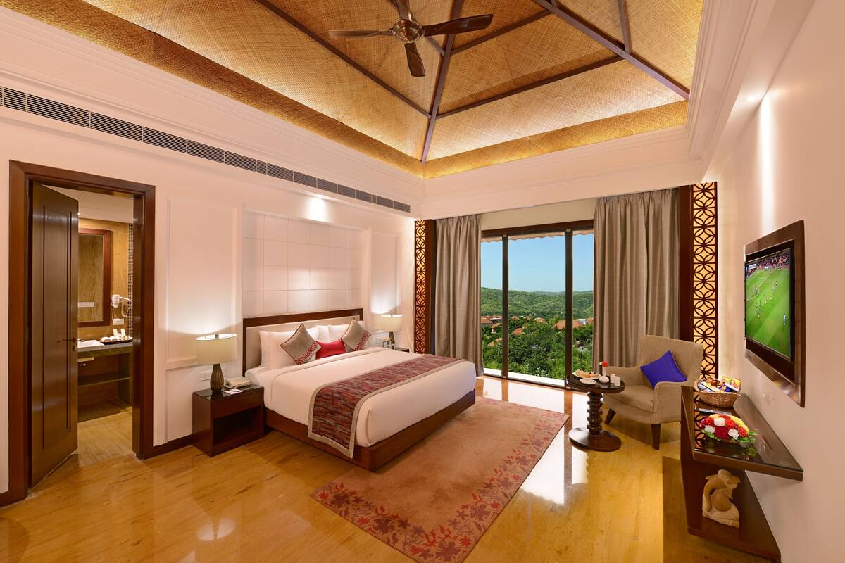A spacious hotel room with a large bed, a television, and a balcony with a view of the landscape.