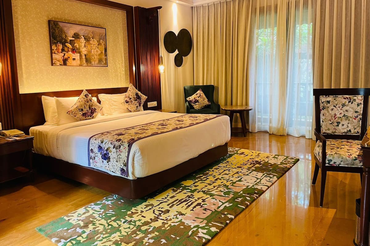 A hotel room with a large bed, a small table, two chairs, a painting on the wall, and a large window with curtains.