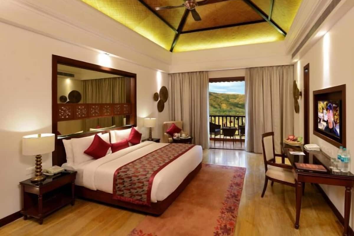 A hotel room with a bed, a desk, a chair, a television, a balcony with a view, and a ceiling fan.