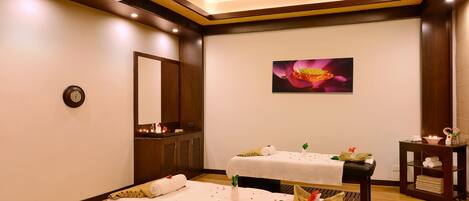 A spa room with two massage tables, a large mirror, a wall-mounted clock, and a framed floral artwork.