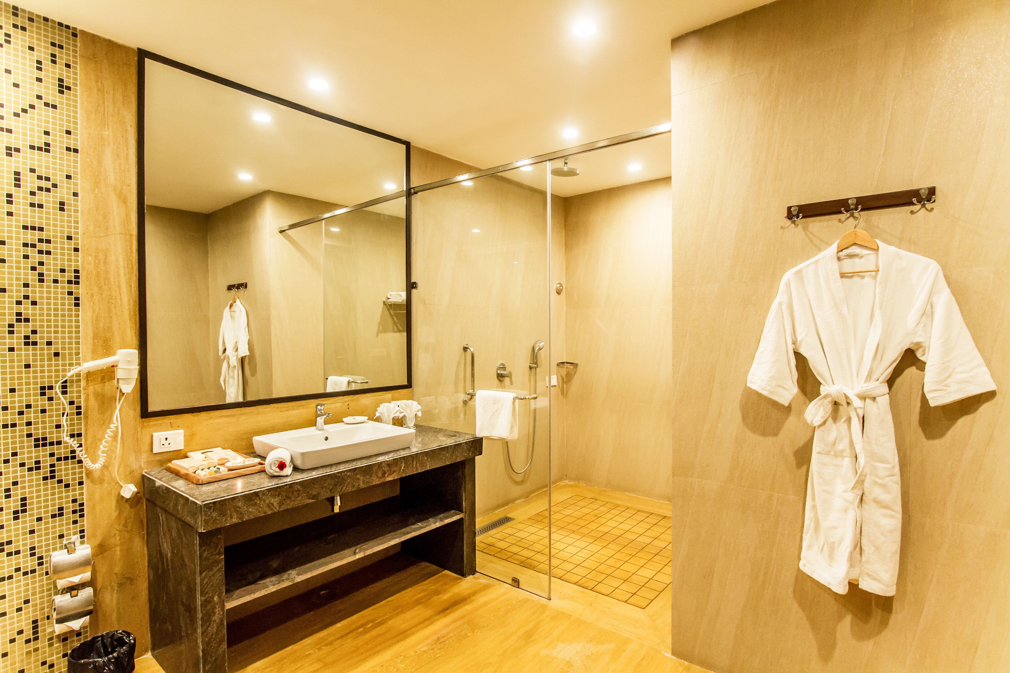 Un baño moderno con un espejo grande, un lavamanos, una ducha y una bata colgada en un perchero.
