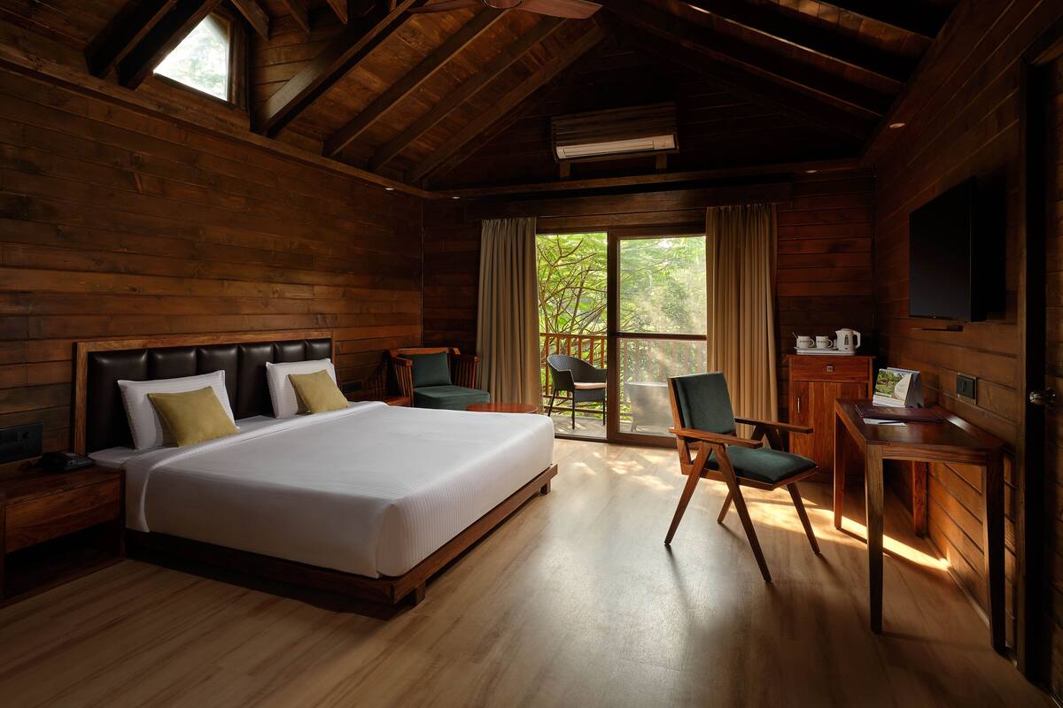 A wooden room with a bed, two chairs, a desk, and a window with curtains.
