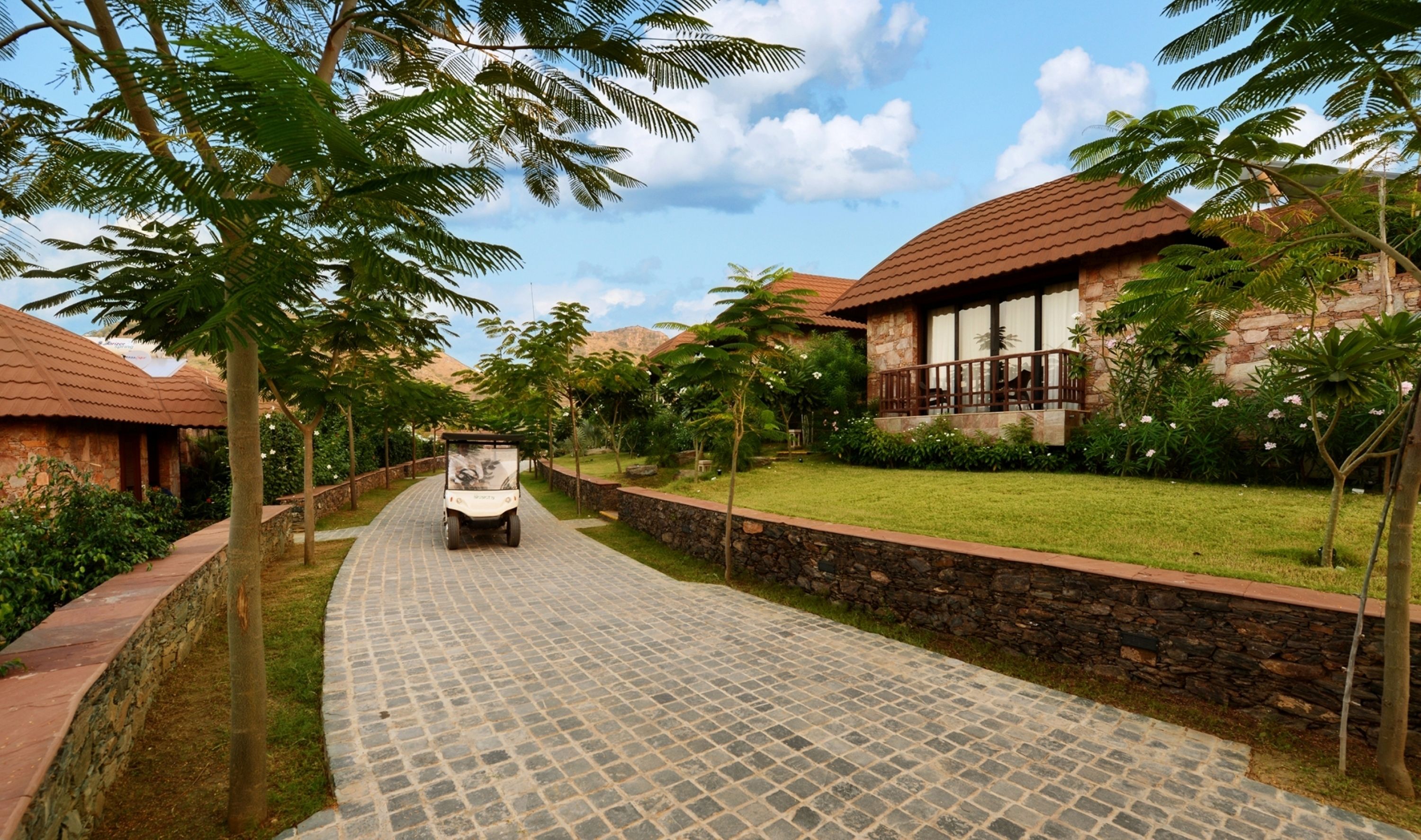 A paved pathway leading to a building with a stone wall and a grassy area.