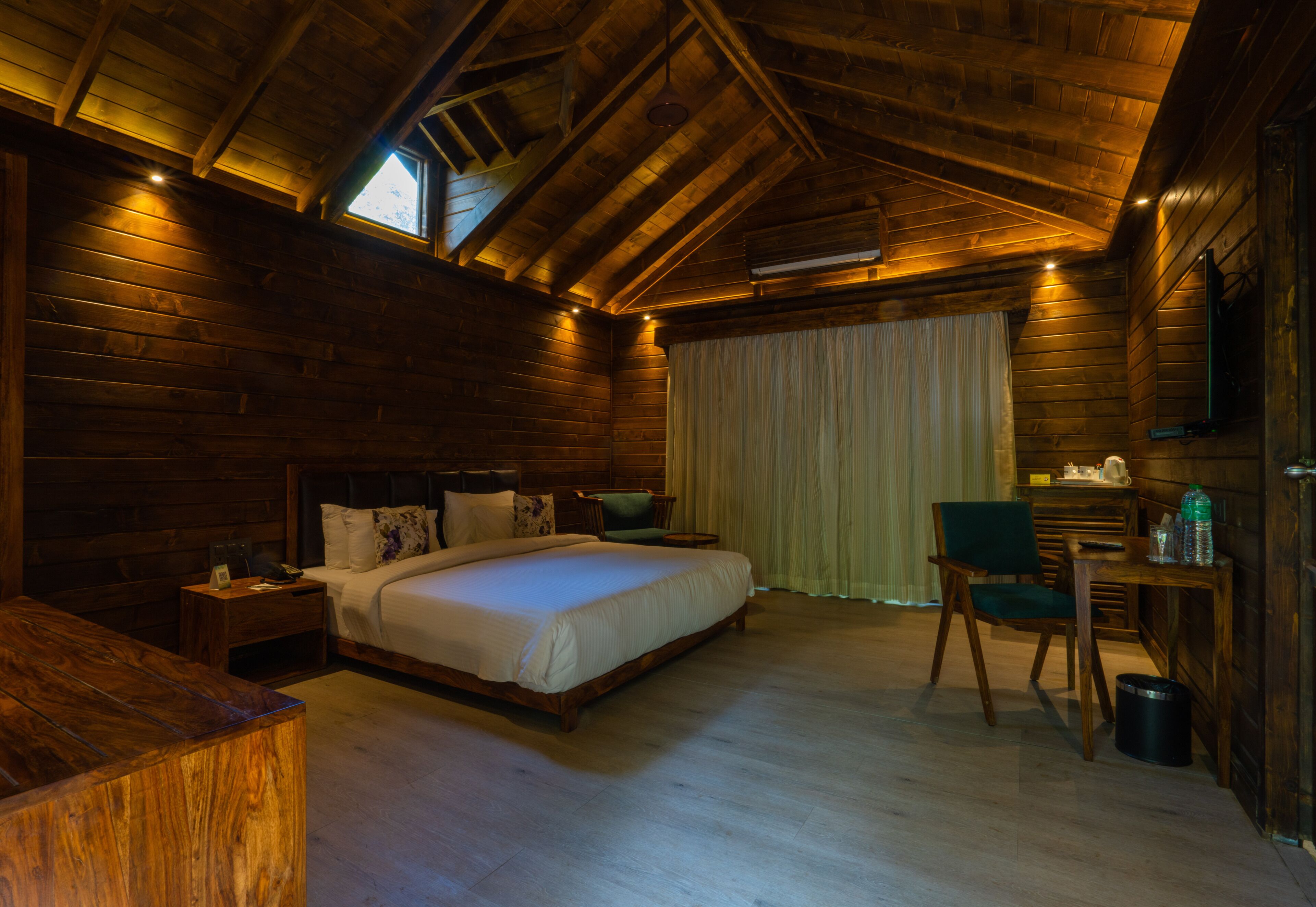 A wooden cabin bedroom with a large bed, a desk, and a chair.