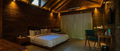 A wooden cabin bedroom with a large bed, a desk, and a chair.