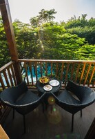 Terraza de madera con dos sillas de mimbre y una pequeña mesa, con vistas a un paisaje verde exuberante y una masa de agua.