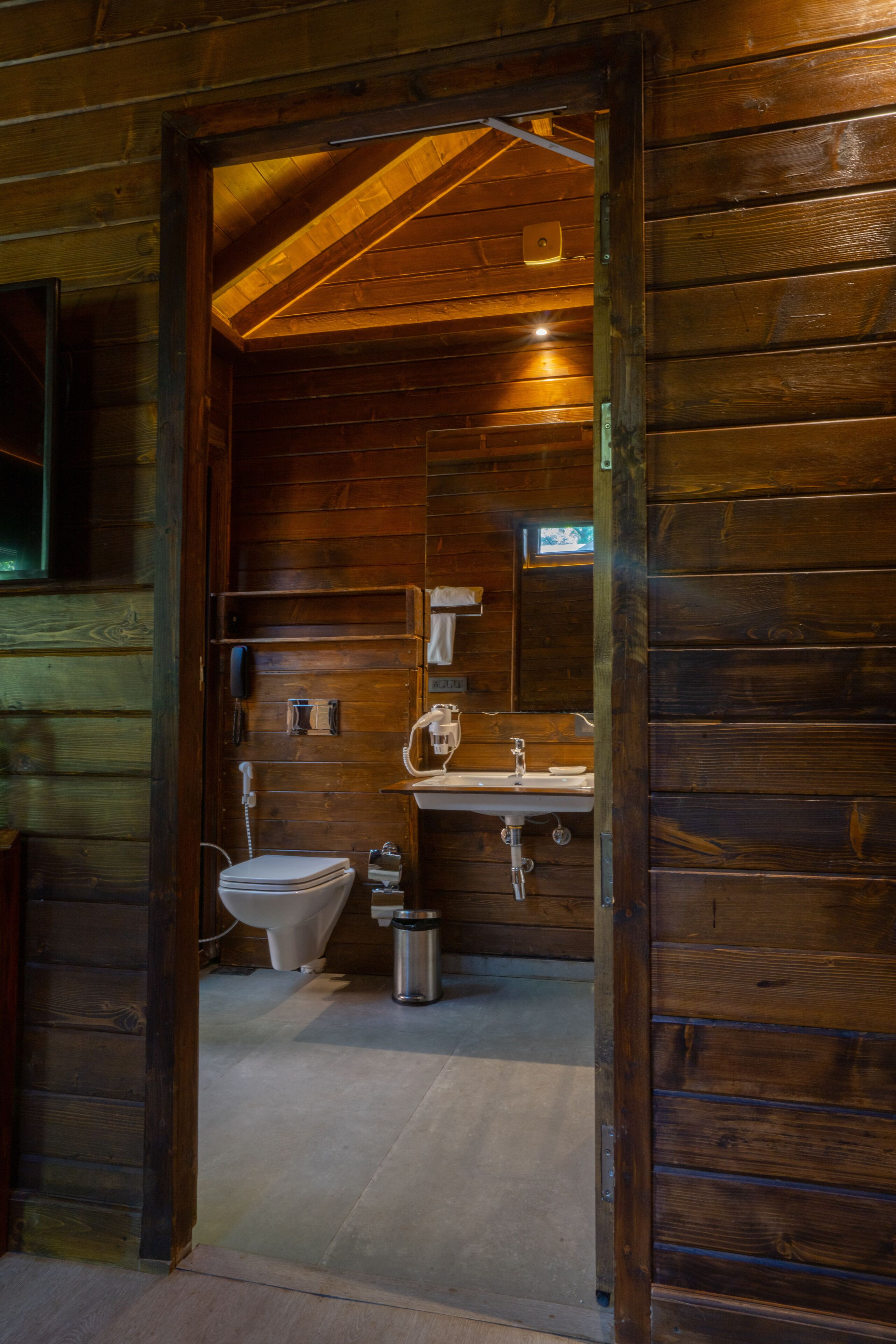 A wooden cabin bathroom with a toilet, sink, and mirror.
