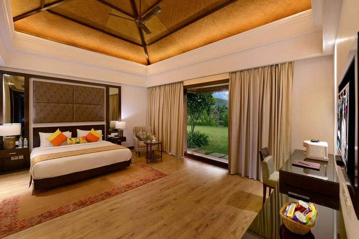 A hotel room with a large bed, a desk, a chair, a window with curtains, a ceiling fan, and a view of the outdoors.