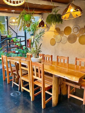 Une table à manger en bois, avec des chaises, entourée de plantes suspendues et agrémentée d’assiettes décoratives fixées au mur.