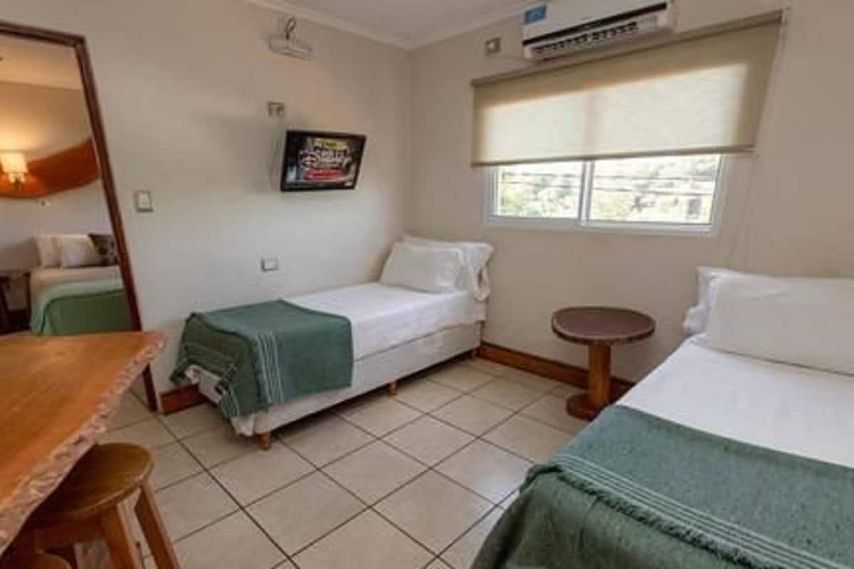 A small, clean room with a bed, a chair, a table, and a window.