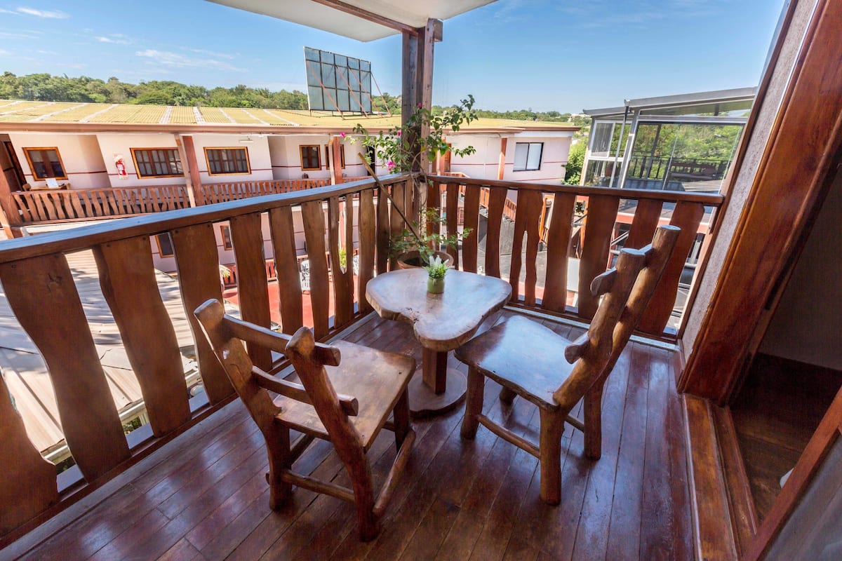A wooden deck with a table and chairs, overlooking a residential area with houses and a clear sky.