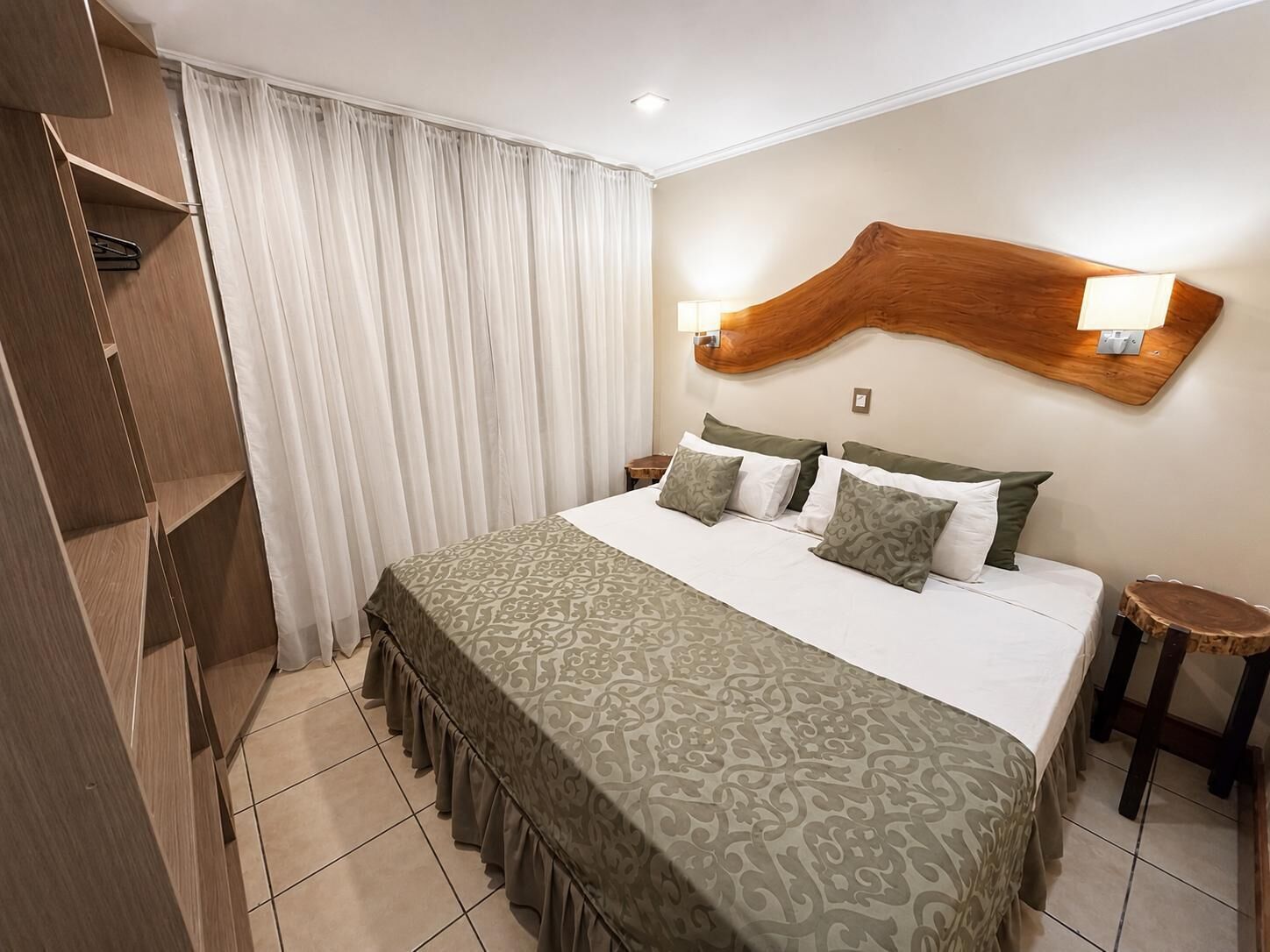 A hotel room with a bed, a wooden headboard, two bedside lamps, a nightstand, and a wardrobe.