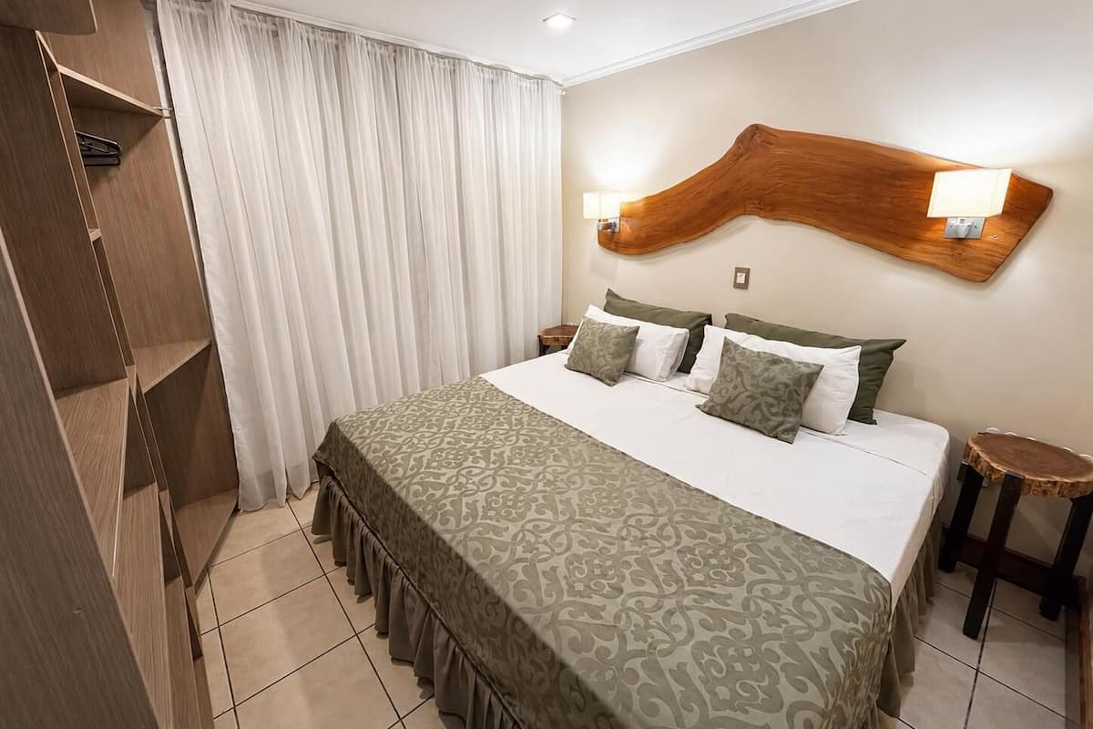 A hotel room with a bed, a wooden headboard, two bedside lamps, a nightstand, and a wardrobe.