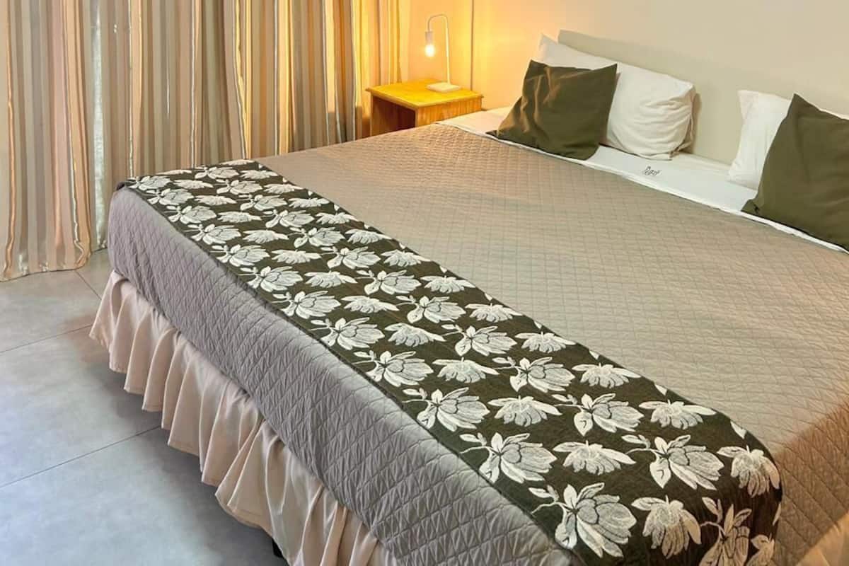 A hotel room with a bed, curtains, a bedside table with a lamp, and a window.